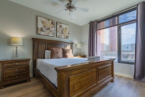 A bedroom with a large bed, two bedside tables, a ceiling fan, and a window with curtains.
