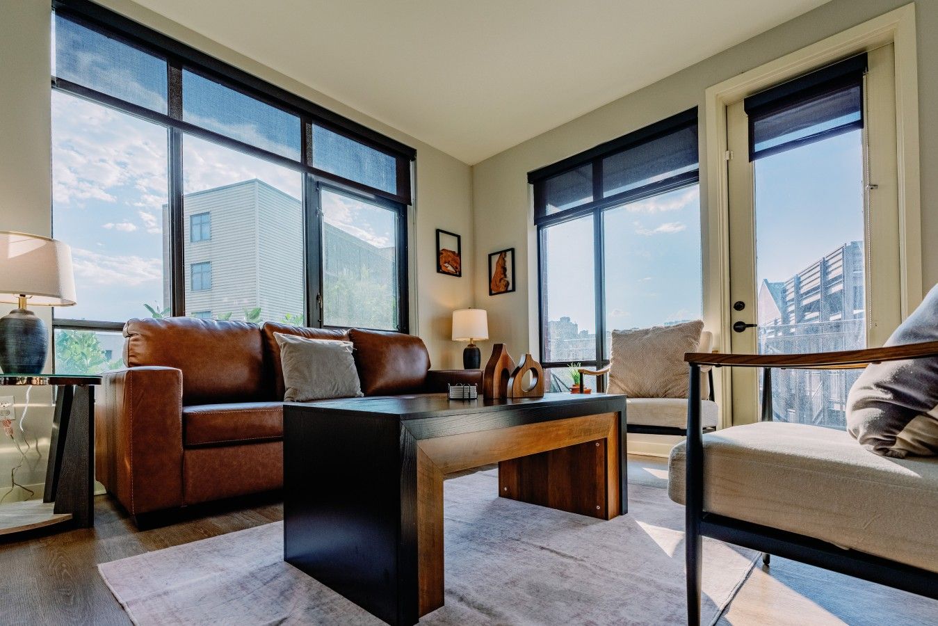 Ein modernes Wohnzimmer mit einem Ledersofa, einem Holztisch und Blick auf die Stadt durch große Fenster.