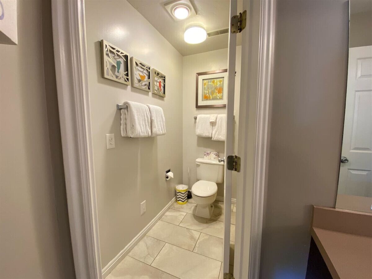 A bathroom with a toilet, a sink, and a mirror. There are towels hanging on the wall and a trash can.