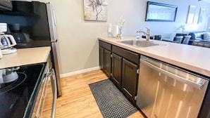 A modern kitchen with stainless steel appliances, a black countertop, wooden flooring, and a black rug. - Inn Building Condo #206 Beautiful updated condo (Garden City)