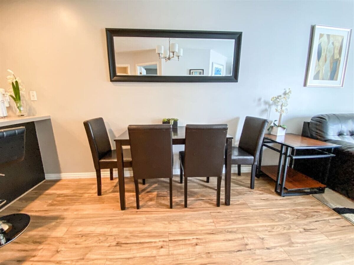 Ein Essbereich mit Holzboden, einem rechteckigen Tisch, vier Stühlen und einem schwarzen Sofa.