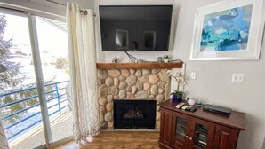 A living room with a stone fireplace, a flat-screen TV mounted above it, and a wooden cabinet to the right. - Inn Building Condo #206 Beautiful updated condo (Garden City)