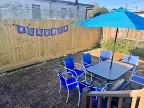 En terrasse med et bord og blå stole, et træhegn og en blå parasol.
