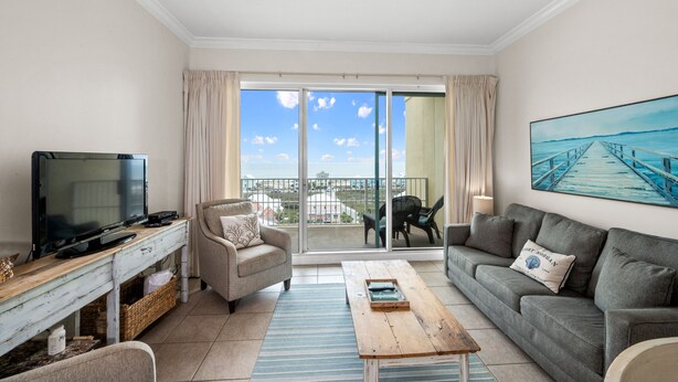 A living room with a TV, sofa, and a balcony with a view. - Indies 704 | 3BR/2BA Penthouse Condo | Sleeps 9 | Gulf Views & Heated Pool (GULF SHORES)