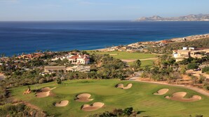 Un campo de golf con búnkeres, un club de campo y vista al océano.