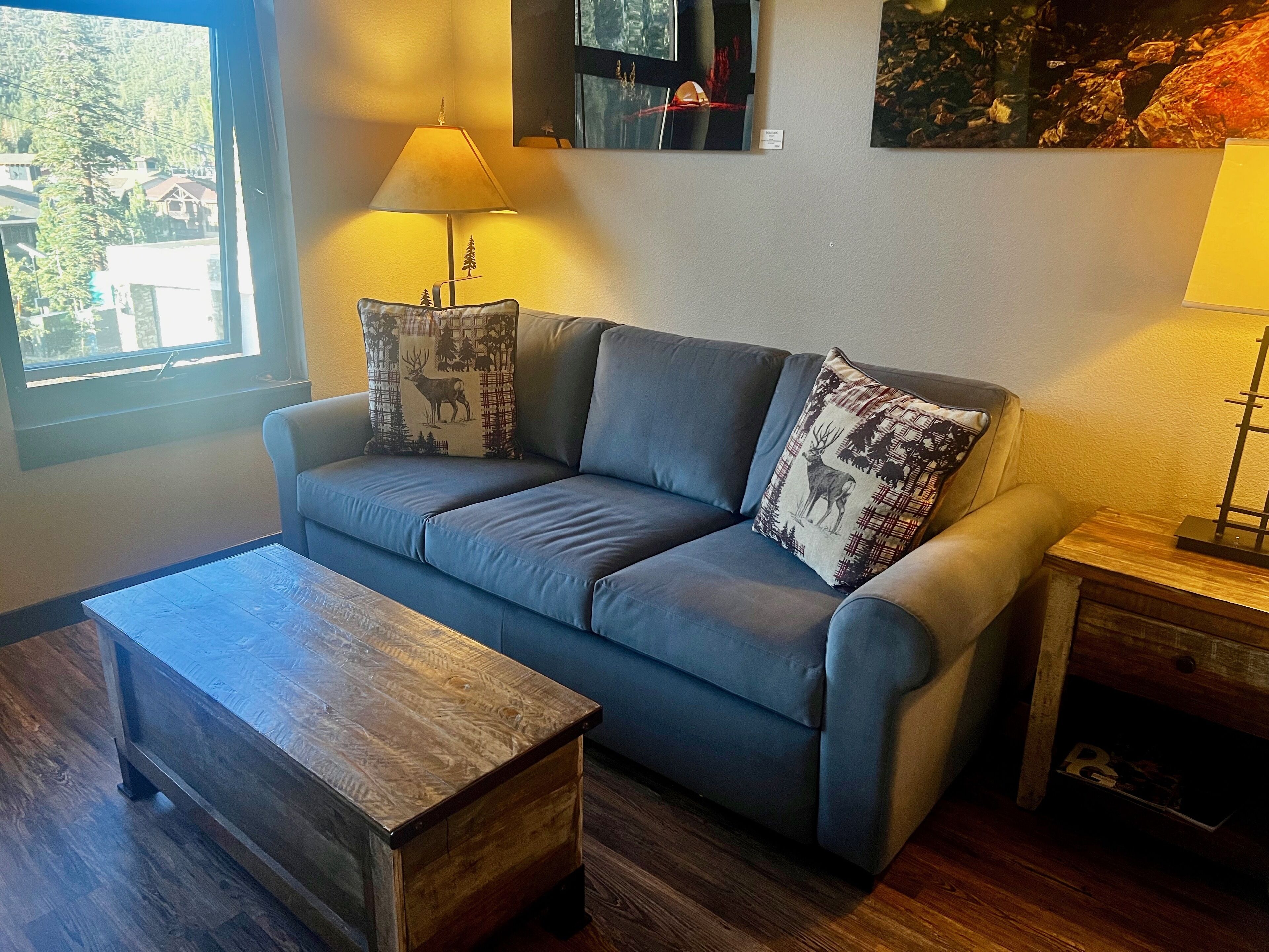 Una sala moderna con un sofá gris, dos almohadones decorativos, una mesa de centro de madera y una lámpara.