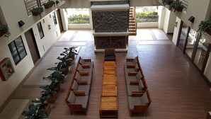 A spacious indoor area with a long wooden bench and sofas arranged for seating, a stone fireplace, and potted plants. - N603 Outlook Ridge Residences (Baguio)