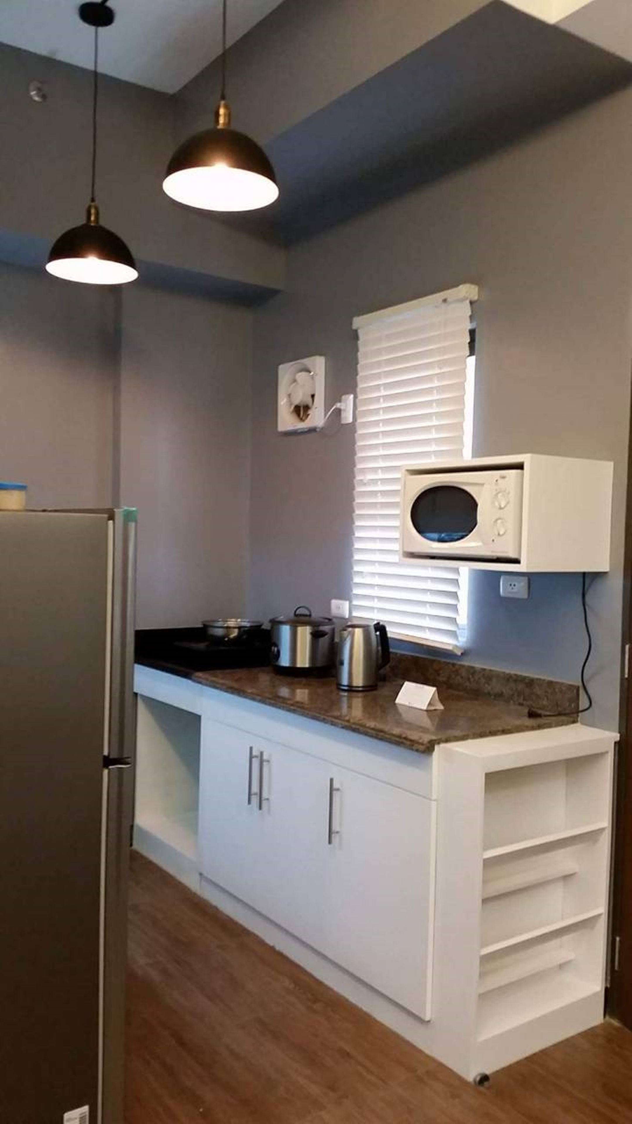Una cocina compacta con refrigerador, microondas y una pequeña encimera con ollas.