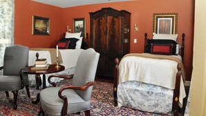 A room with a bed, two armchairs, a wooden cabinet, and a small table with a book and candle. - Cedar Lane Plantation dated back to early 1809 (New Kent)