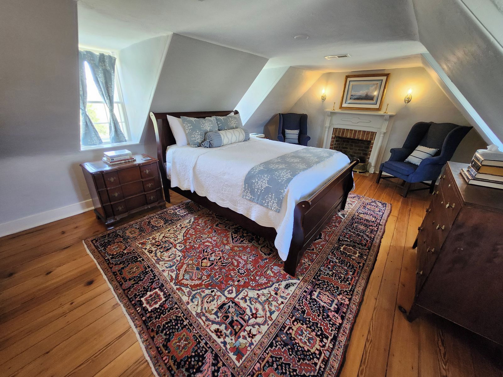 A bedroom with a large bed, a fireplace, a chair, and a dresser.