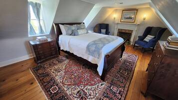 A bedroom with a large bed, a fireplace, a chair, and a dresser.