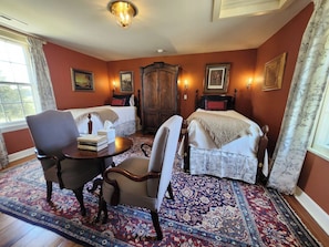 Una habitación con dos camas, un armario de madera, una mesa con libros y una alfombra estampada.