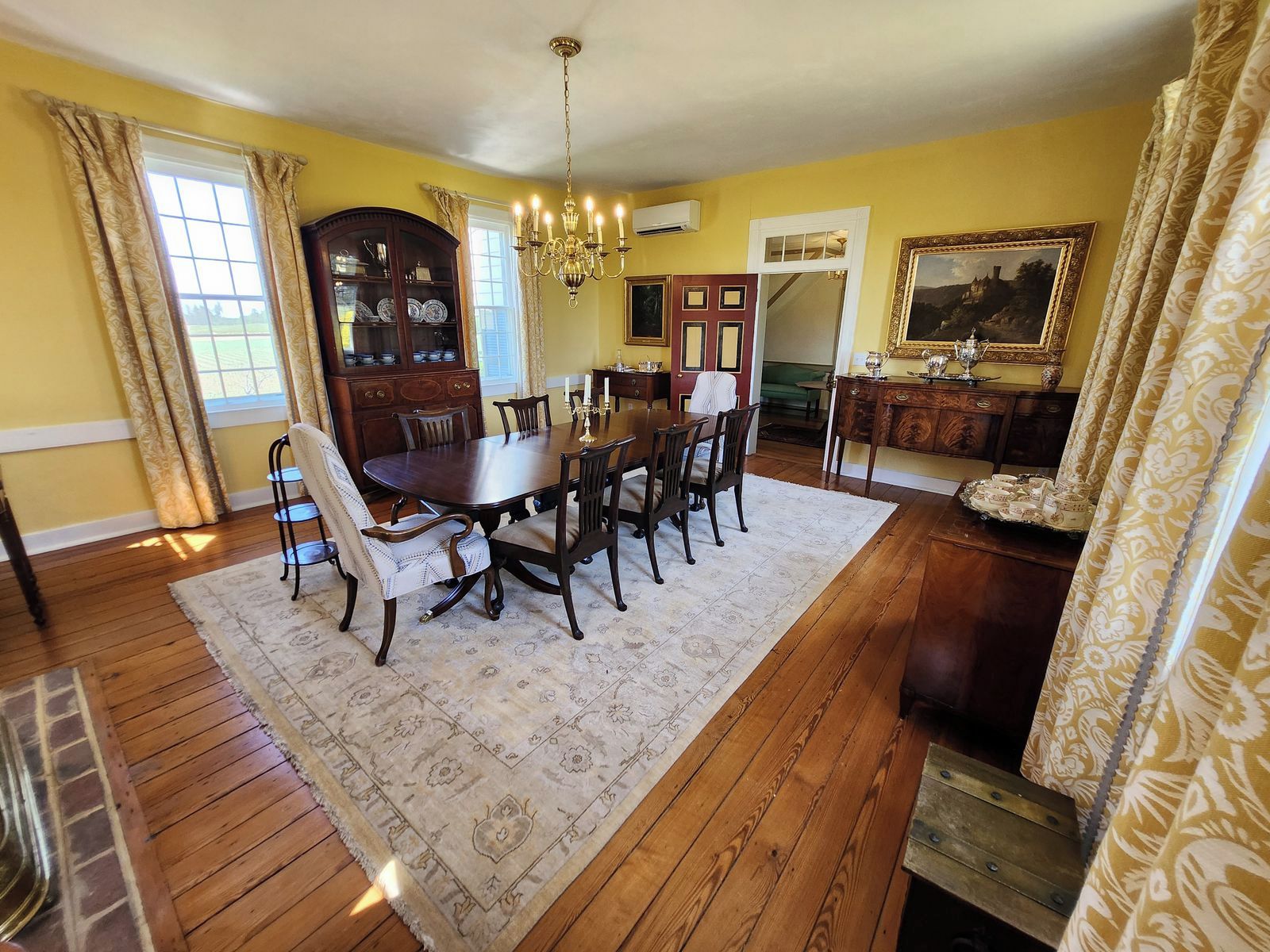 A dining room with a wooden table, chairs, a chandelier, and a patterned rug.