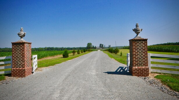 A gravel road leading to a white gate with brick pillars and a sign. - Cedar Lane Plantation dated back to early 1809 (New Kent)