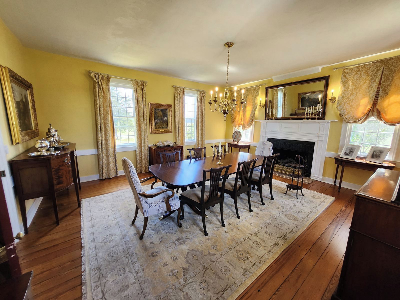 A dining room with a wooden table, chairs, a chandelier, and a fireplace.