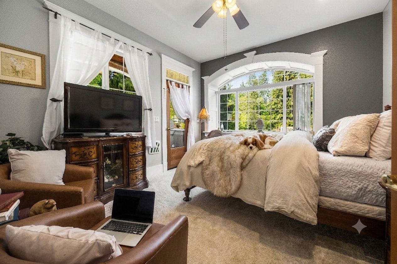 A bedroom with a bed, a television, a laptop, and a window with a view of greenery.