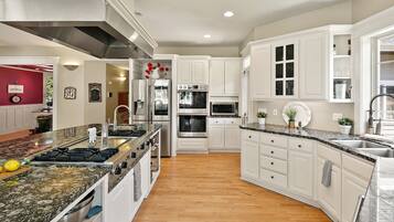 A modern kitchen with white cabinetry, granite countertops, stainless steel appliances, and a wooden floor.