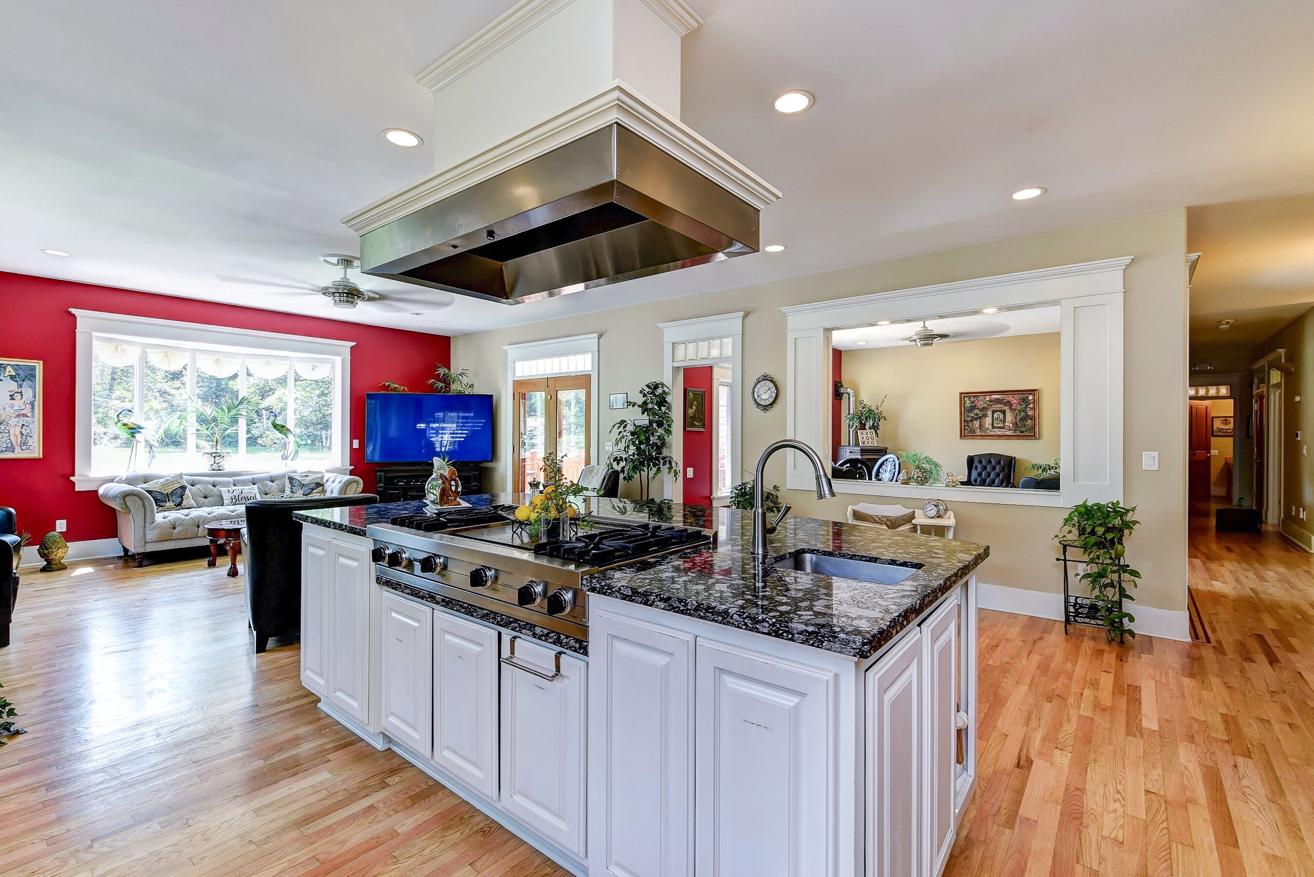 A spacious kitchen with white cabinetry, a large island, and a stainless steel range hood.