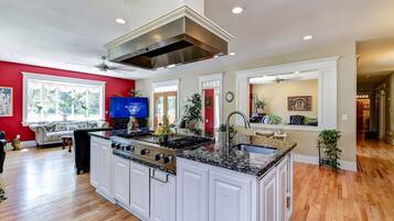 A spacious kitchen with white cabinetry, a large island, and a stainless steel range hood.