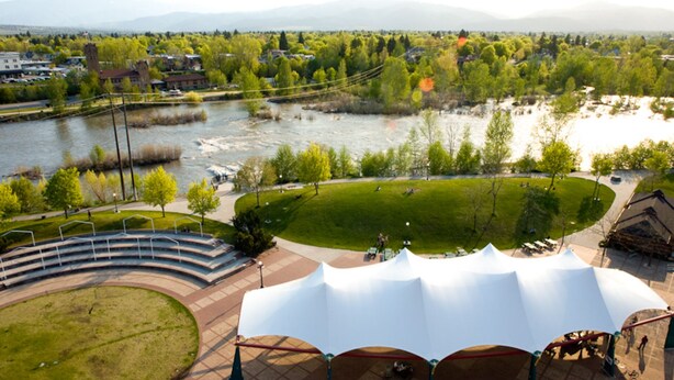 A riverside park with a stage, seating, and a tent.