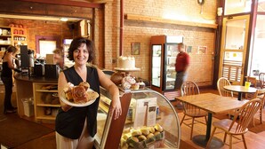 A bakery with a display case of baked goods, a counter with a person serving, and a brick wall interior.