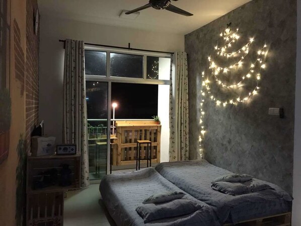 Un dormitorio con una cama, ventilador de techo, ventana con cortinas y luces de hadas en la pared.