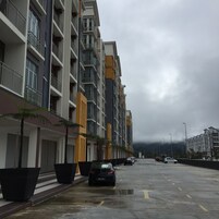 Un edificio residenziale a più piani con balconi, un'area di parcheggio e una strada bagnata.