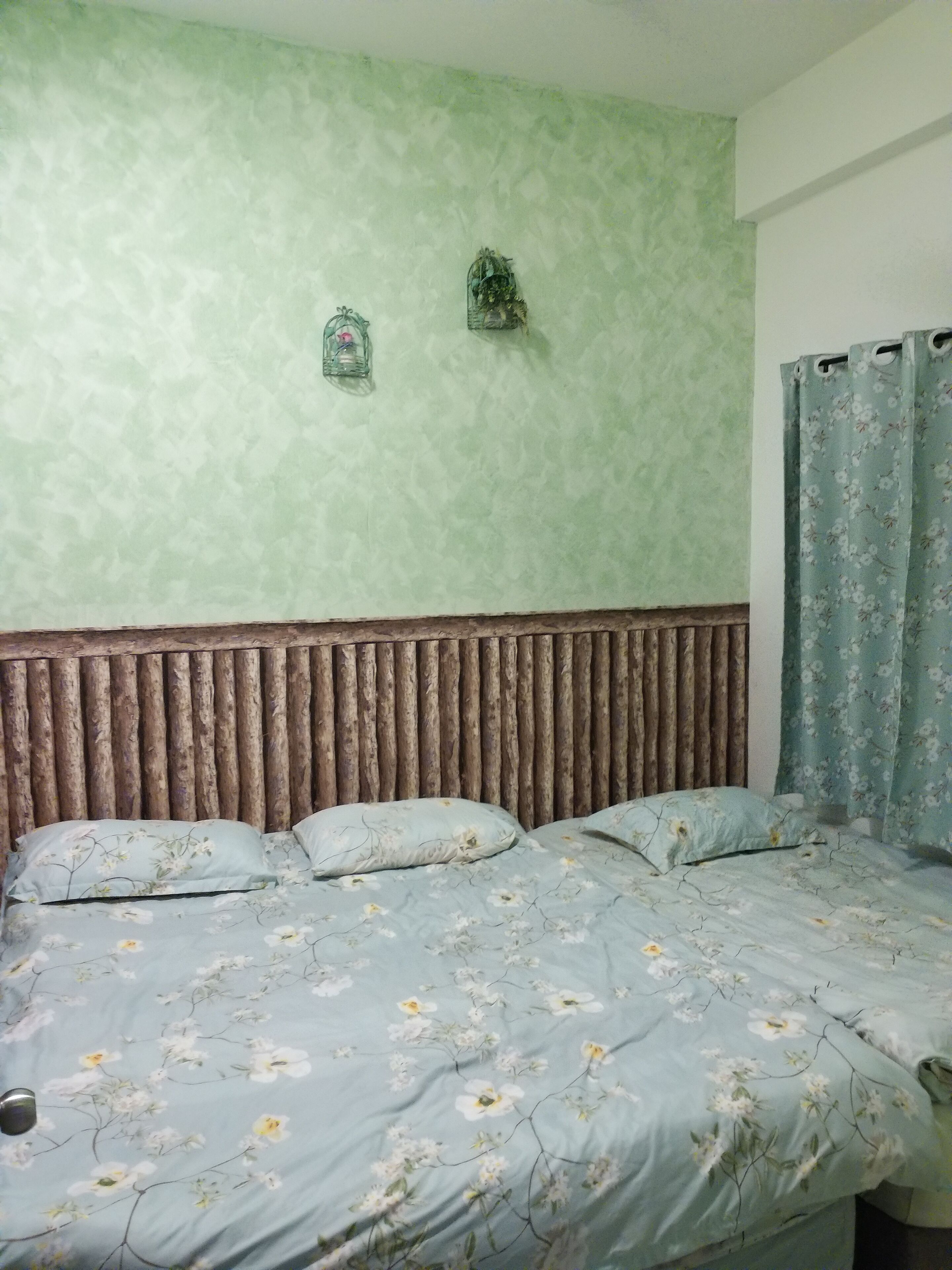 A bedroom with a bed, floral bedding, a green textured wall, and a wooden headboard.