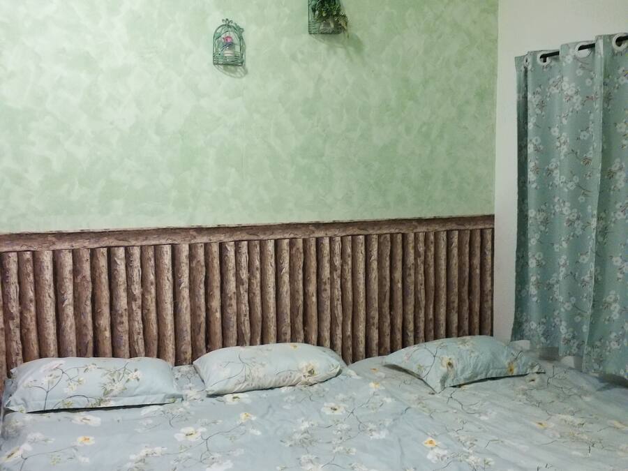 A bedroom with a bed, floral bedding, a green textured wall, and a wooden headboard.