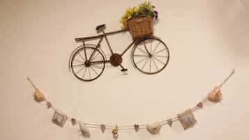 Une décoration murale représentant un vélo avec un panier rempli de fleurs et une guirlande d’ornements en forme de cœur.