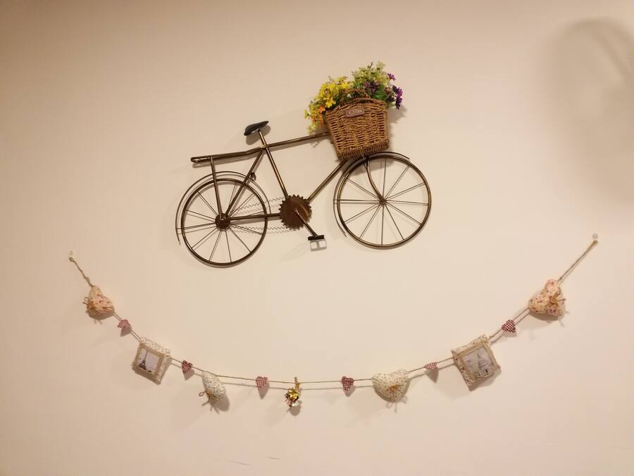 Une décoration murale représentant un vélo avec un panier rempli de fleurs et une guirlande d’ornements en forme de cœur.