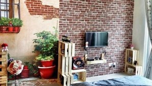 Una habitación con pared de ladrillo, un reloj montado, un ventilador de techo y un televisor en la pared.