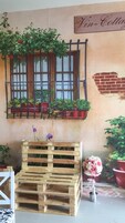 Un interior rústico con un banco de palets de madera, una ventana con plantas en macetas y un letrero que dice "Vin-Cottage".