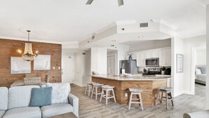 Un vaste espace de vie agrémenté d’un mur d’accent en bois, d’un îlot central avec des tabourets de bar et d’une cuisine moderne en arrière-plan.