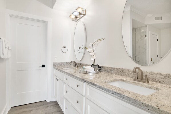 Un baño moderno con lavamanos doble, muebles blancos, un espejo grande y un aplique en la pared.