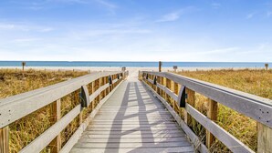 Une promenade en bois menant à une plage, avec un ciel dégagé.