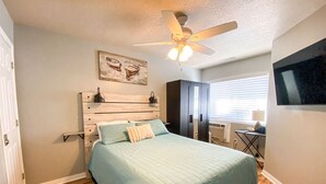A bedroom with a bed, a ceiling fan, a TV mounted on the wall, and a window with blinds. - Beautiful Inn Building Condo #208 Pet friendly (Garden City)