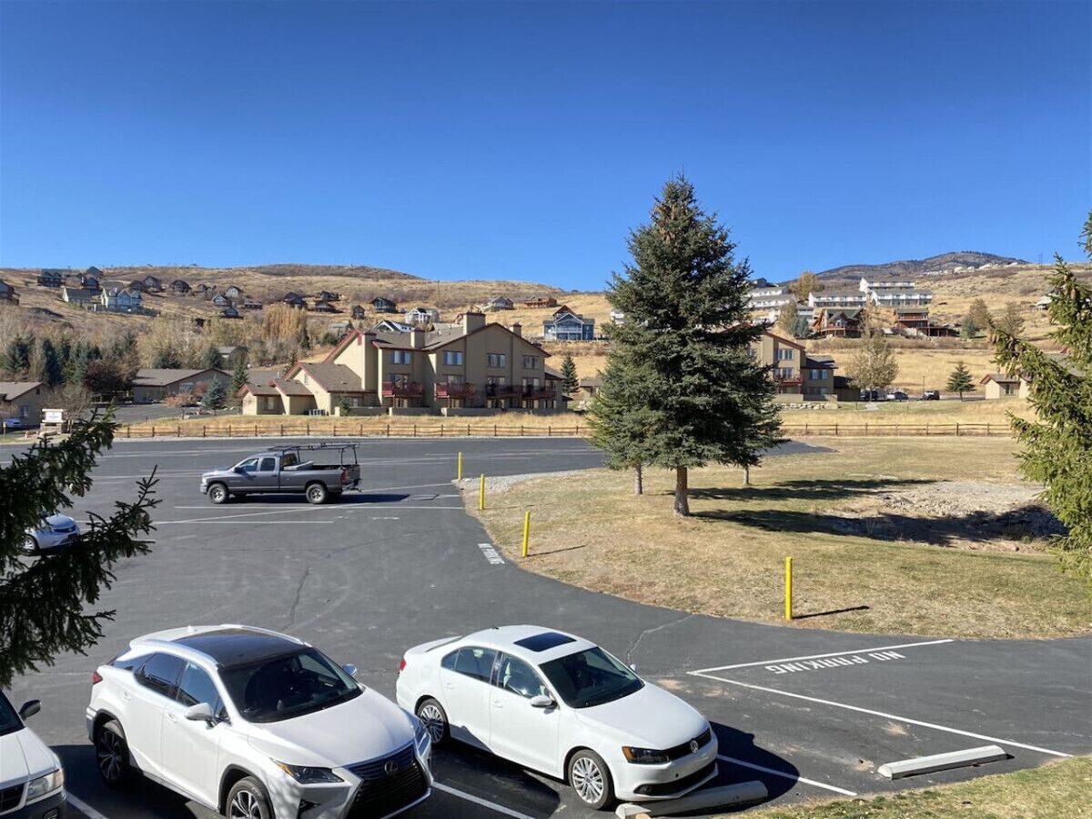Un estacionamiento con varios coches, cielo despejado y un área residencial con casas al fondo.