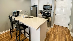A compact kitchen with a central island, white cabinets, a stainless steel refrigerator, a microwave, and a stove. - Beautiful Inn Building Condo #208 Pet friendly (Garden City)