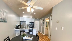 A modern kitchen with white cabinets, a central island, and a dining area with a round table and chairs. - Beautiful Inn Building Condo #208 Pet friendly (Garden City)