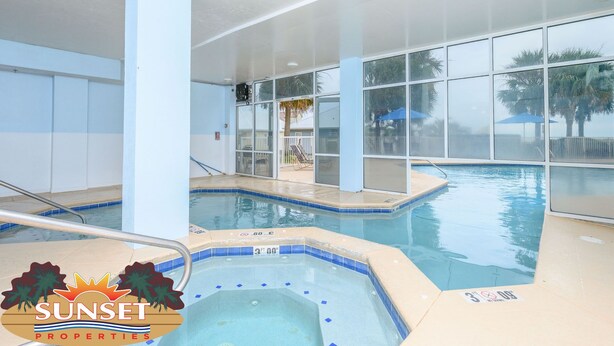Una piscina interior con paredes de vidrio transparente, un jacuzzi y vistas a palmeras afuera.