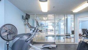 Un gimnasio con cintas de correr, una bicicleta estática y un ventilador.