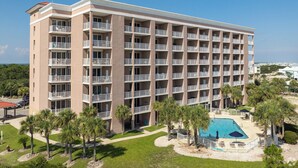 Un hotel de varios pisos con balcones, piscina y palmeras.