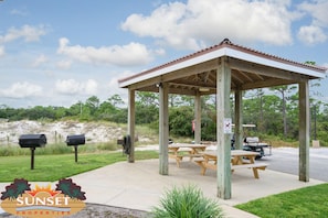 Relax in a serene gazebo with a picnic table and barbecue grills nearby, surrounded by lush greenery and a golf course.