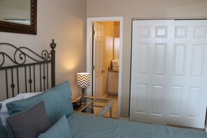 Een slaapkamer met een bed, kussens, een nachtkastje met een lamp, een spiegel en een kledingkast.