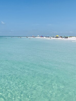 Una playa con agua turquesa cristalina, arena blanca y varias sombrillas.