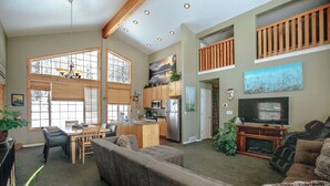 A spacious living room with a large sofa, dining area, kitchen, and a balcony with wooden railings.