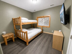 Une chambre avec un lit superposé, une petite table de chevet, une commode et un téléviseur fixé au mur.