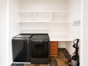 A laundry room with two stacked washers and dryers, a wooden cabinet, and a vacuum cleaner. - Great Western by Cottonwood Lodging (Brighton)