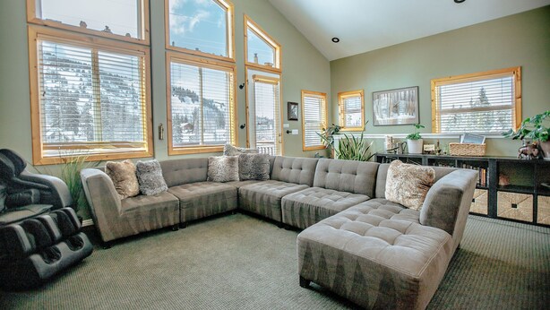 A spacious living room with a sectional sofa, large windows, and a ceiling fan.